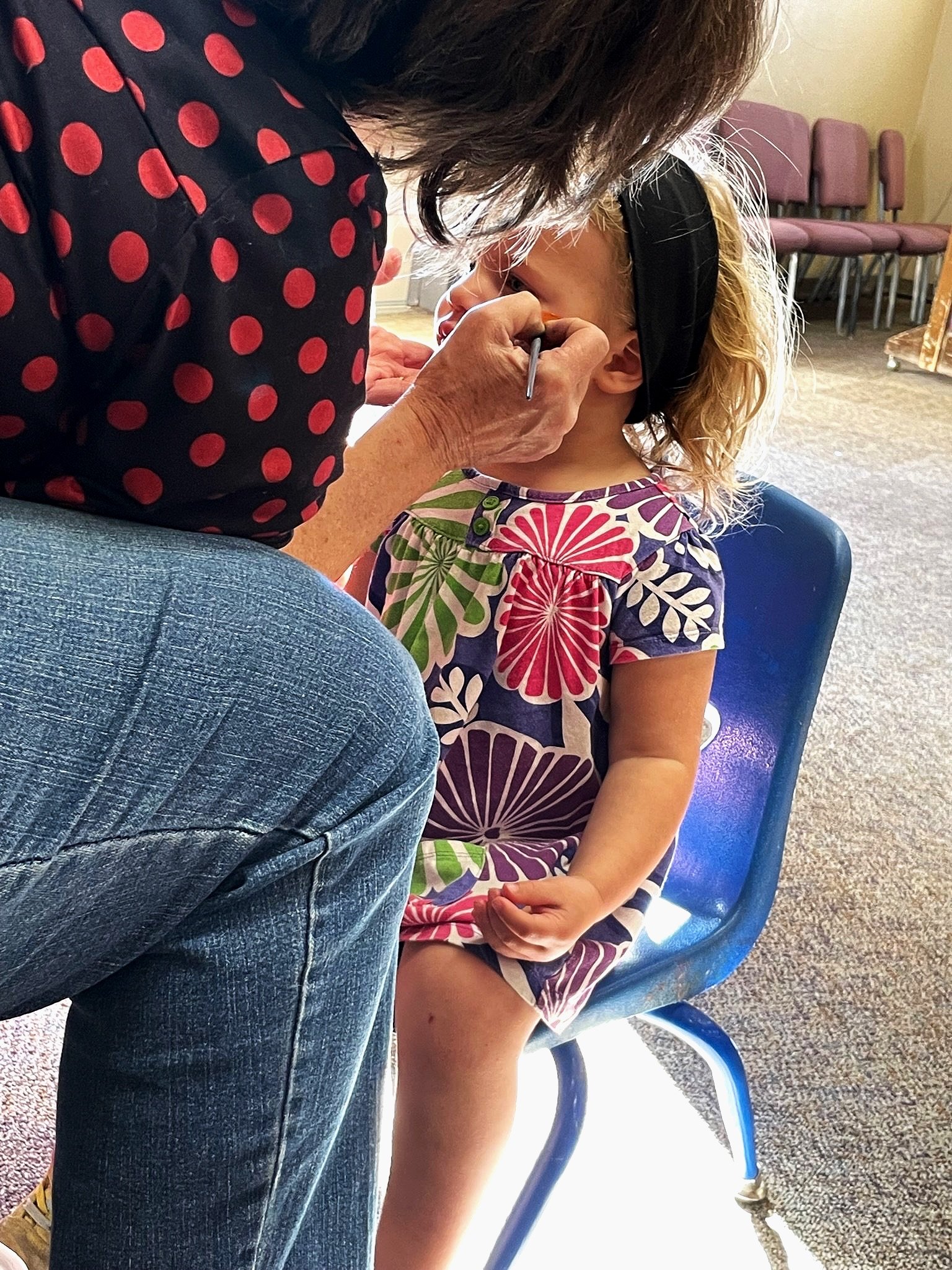 A child having their face painted at a parish gathering.
